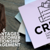 There is a stack of post-its to the right of the picture with a graphic relating to customer relationship management on the topmost one. To the bottom left is the title, "6 Advantages of Customer Relationship Management," and there is a smiling lady in pink peeking out from the left side of the picture.